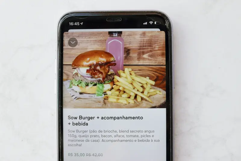 Celular aberto na tela do iFood, o app de tudo, com uma imagem de um combo de hambúrguer e fritas.