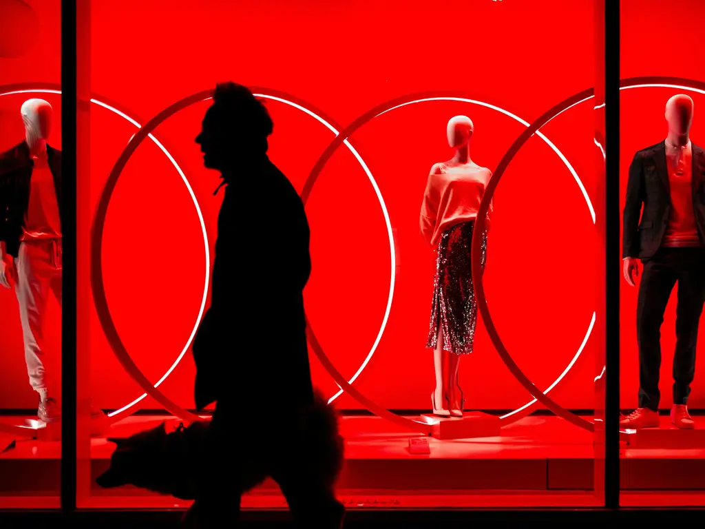 Homem passa em vitrine vermelha com manequins vestidas com roupas da estação.
