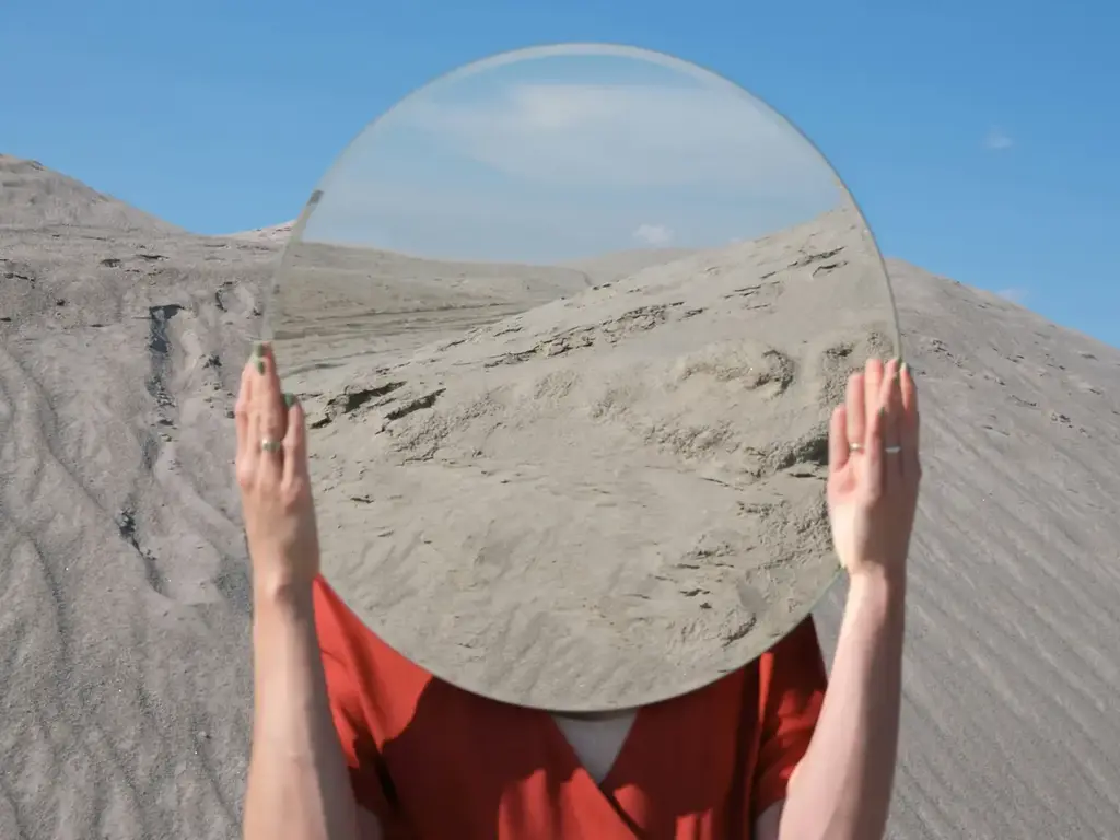Mulher no deserto com espelho na cabeça, refletindo a imagem do ambiente. 
